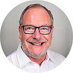 A smiling middle-aged man with glasses and a light-colored shirt, showcasing a friendly and approachable expression.