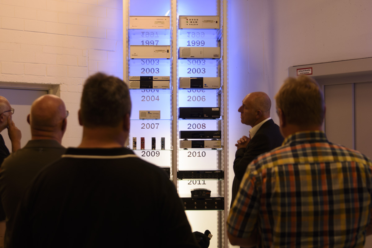 A group of people observes a display featuring various technology devices arranged by year, highlighting advancements from 1997 to 2011.