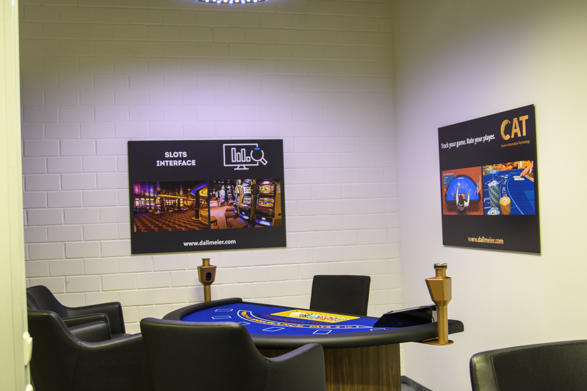 A gaming room featuring a table with a blue felt surface, surrounded by black chairs. Two informative posters are displayed on the walls.