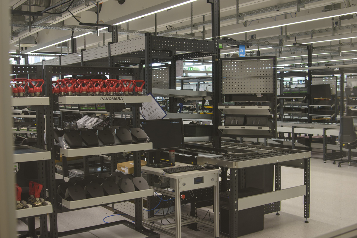 A spacious manufacturing facility featuring shelves with equipment and tools, including red-handled tools and black components, arranged for assembly or storage.