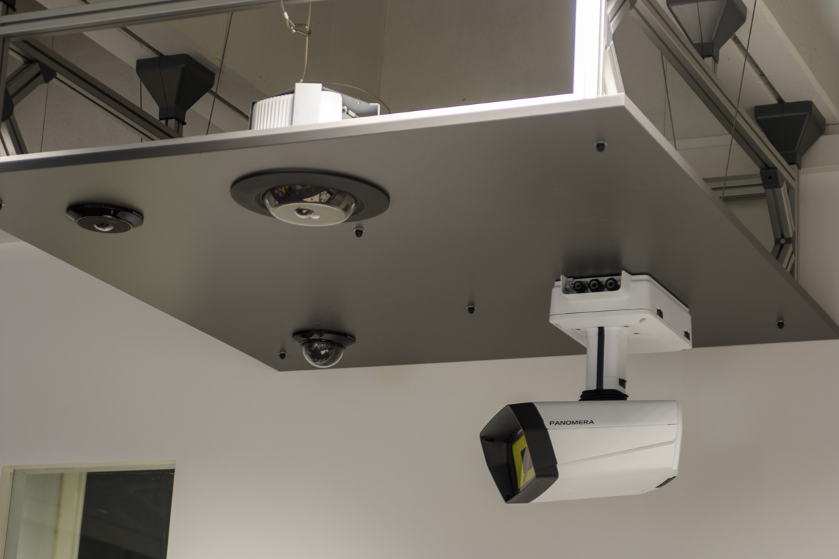 Ceiling-mounted surveillance and projection devices, including cameras and a projector, attached to a flat surface in an indoor setting.