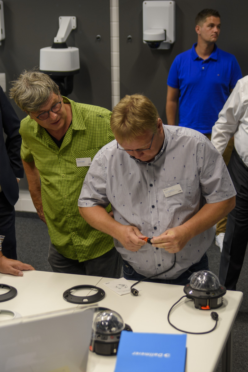 A group of individuals are gathered around a table, focused on assembling or working with equipment. One person is using tools, while others observe and engage in conversation.