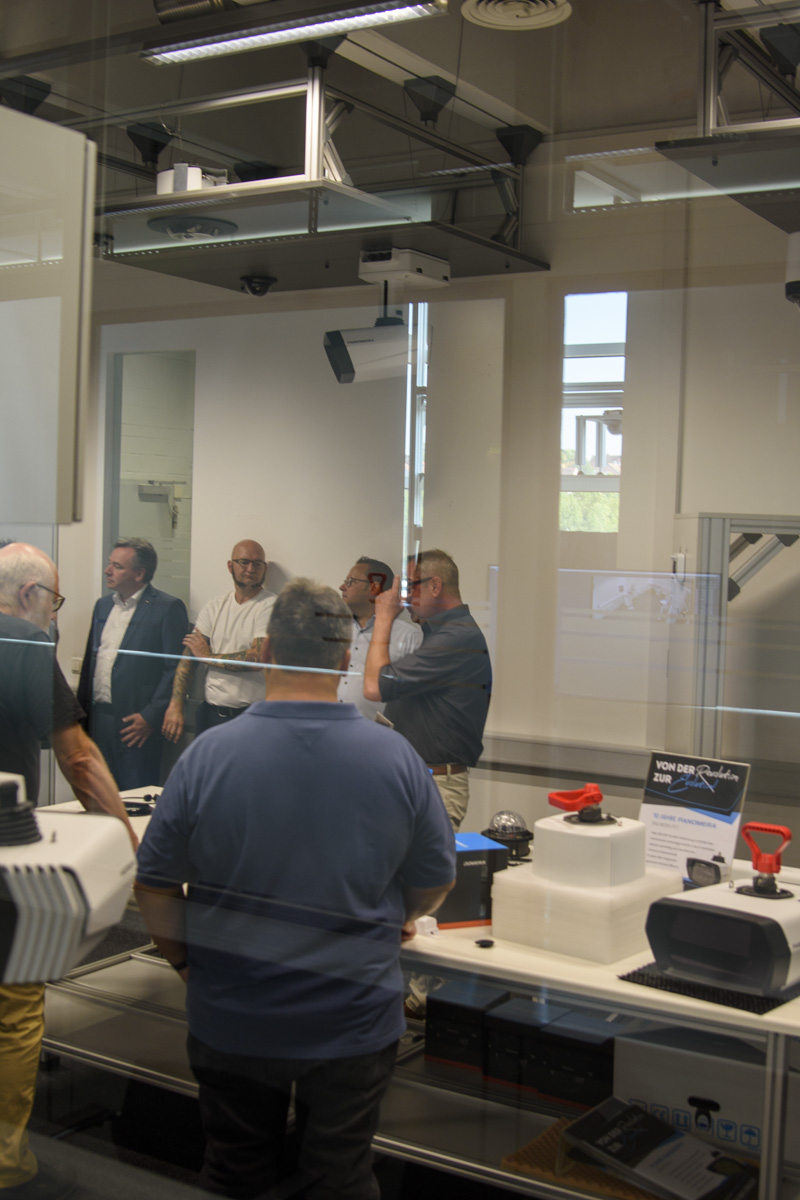 A group of people discussing around a table in a modern, well-lit room, with various gadgets and equipment visible in the foreground.
