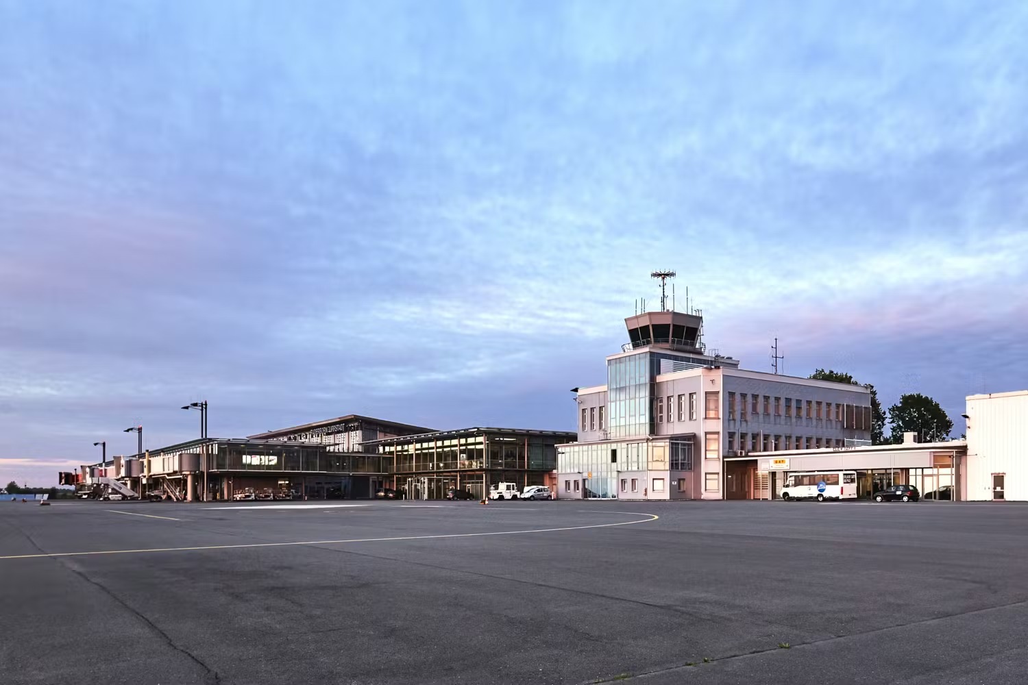 An airport building featuring a tower, modern terminals, and an expansive tarmac under a cloudy sky, showcasing a blend of traditional and contemporary architecture.