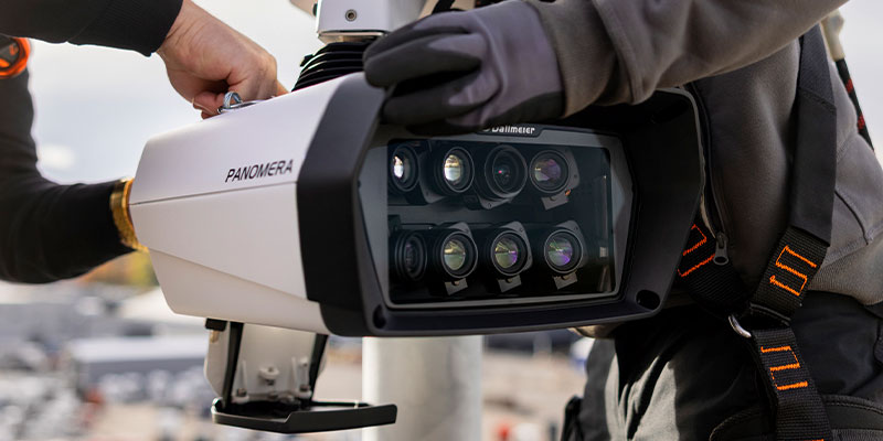 A close-up of a person attaching a multi-lens camera system to a support structure, showcasing the Panomera's intricate lens arrangement and robust design.