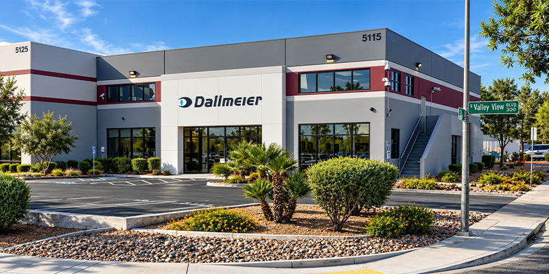 A modern commercial building with the sign "Dallmeier" prominently displayed. The structure features large windows and landscaping in the foreground, with a clear blue sky above.