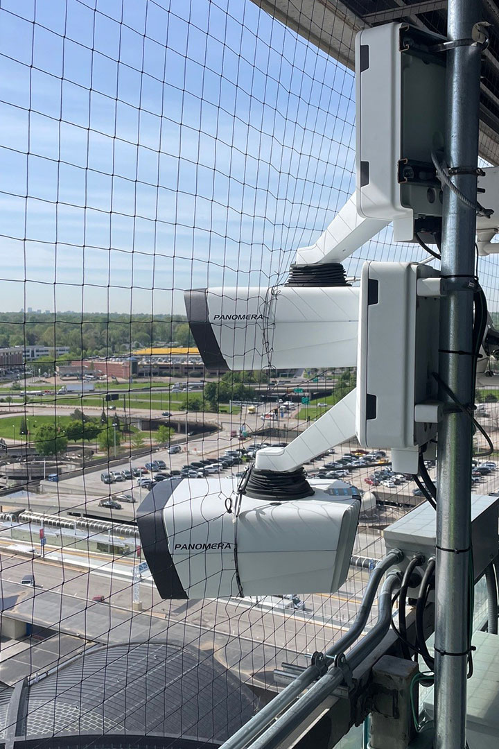 Alt text: Three surveillance cameras mounted on a building, overlooking a busy urban area with roads and vehicles.