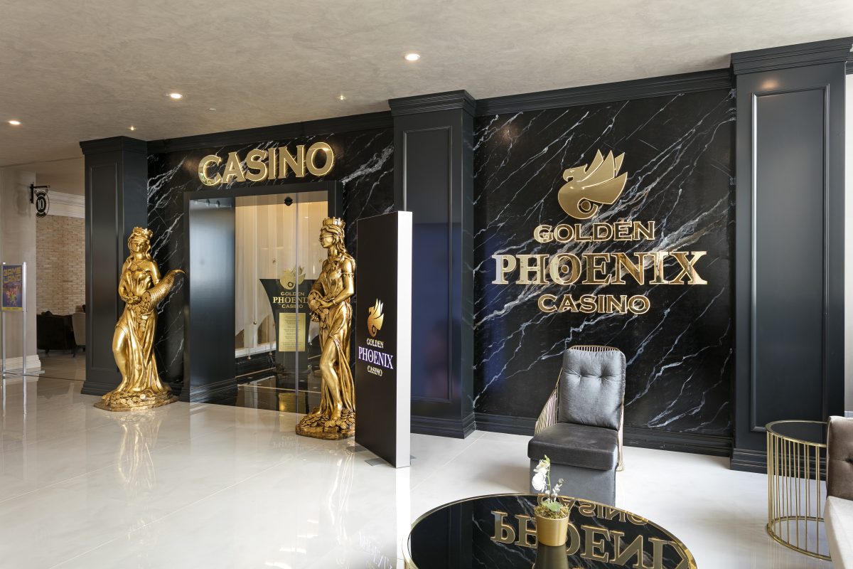 Interior of the Golden Phoenix Casino featuring a glossy black wall with gold accents, two golden statues, and a seating area with a modern chair.